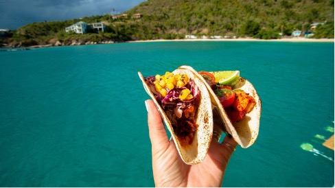 A person holding tacos in front of a sea